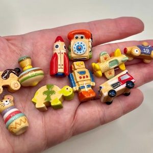 May include: A collection of miniature wooden toys, including a dog, spinning top, rocket, telephone, airplane, race car, robot, turtle, mouse, and a small truck. The toys are painted in various colors and designs.
