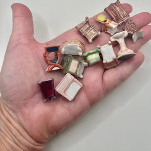 May include: A collection of miniature ceramic furniture pieces, including chairs, tables, and a pedestal. The pieces are painted in various colors, such as brown, white, red, and green. The furniture is small, with intricate details.