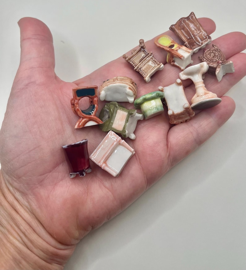 May include: A collection of miniature ceramic furniture pieces, including chairs, tables, and a pedestal. The pieces are painted in various colors, such as brown, white, red, and green. The furniture is small, with intricate details.