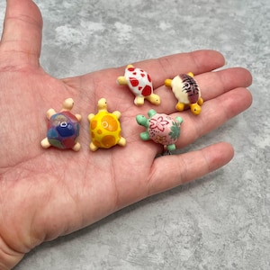 May include: Five miniature turtle figurines with colorful designs. The turtles have various patterns, including red spots, yellow polka dots, and floral prints. Each turtle is approximately 1 inch in length.