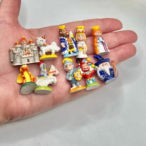 May include: A collection of miniature ceramic figurines, including a castle, a unicorn, a king, a queen, a wizard, a knight, a jester, and a dragon. The figurines are brightly colored and detailed, with a whimsical aesthetic.