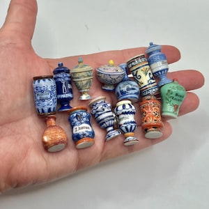 May include: A collection of miniature ceramic apothecary jars and vases in various shapes, colors, and patterns. The pieces feature intricate hand-painted designs, some with legible text labels like Muria, Z.boran, and Laxativ, showcasing a variety of styles.