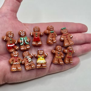 May include: A collection of miniature gingerbread man figurines with various colorful outfits and accessories. The gingerbread men are brown with white icing details, and some have red, green, and yellow accents. The figurines are small, measuring approximately 1 inch in height.