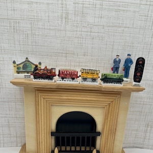 May include: A decorative fireplace mantel displays miniature train cars, a locomotive, and figurines. The train cars are red, yellow, and green. The locomotive is red and black. The figurines are of train conductors.