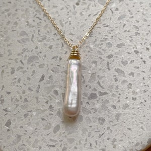 May include: A gold chain necklace with a single, long, white pearl pendant.