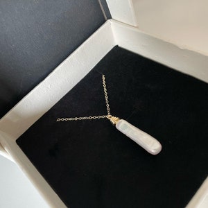 May include: A gold chain necklace with a long, white pearl pendant. The necklace is in a black velvet box.