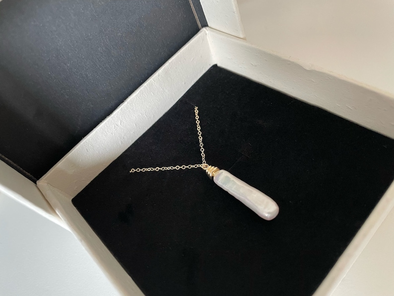 May include: A gold chain necklace with a long, white pearl pendant. The necklace is in a black velvet box.