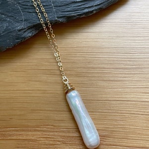 May include: A long, white pearl pendant necklace with a gold chain and a gold clasp. The pearl is iridescent and has a smooth, oval shape.