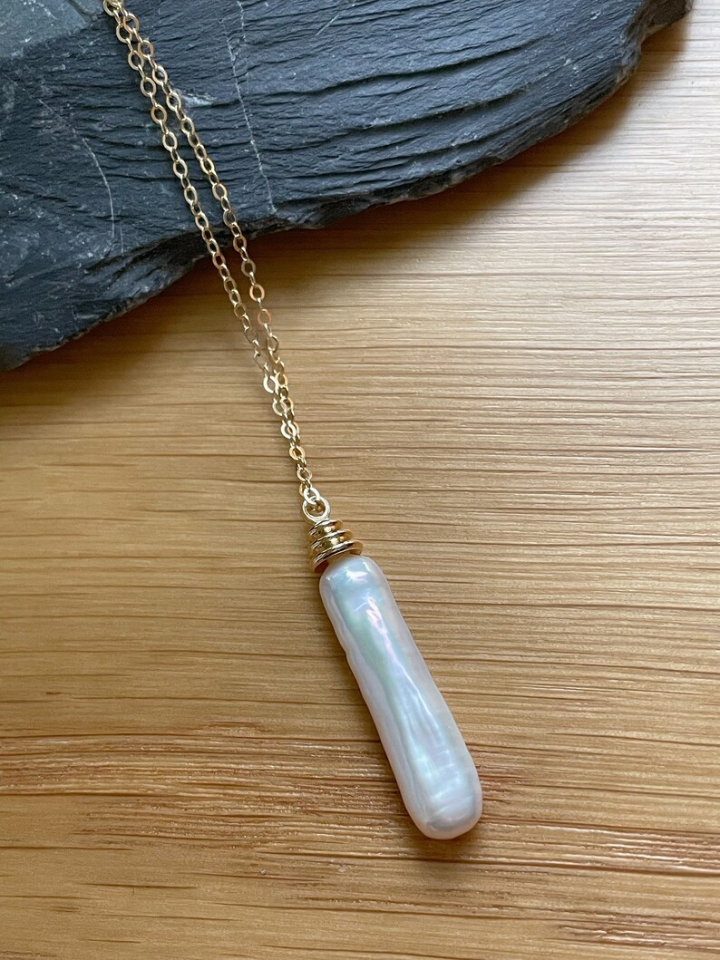 May include: A long, white pearl pendant necklace with a gold chain and a gold clasp. The pearl is iridescent and has a smooth, oval shape.