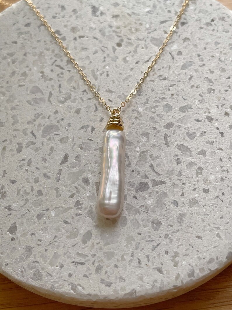 May include: A gold chain necklace with a single, long, white pearl pendant.