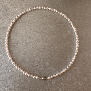 May include: A delicate pearl necklace with a silver clasp. The necklace is composed of numerous small, round, white pearls, strung together to form a complete circle. The clasp is a small, silver-colored metal piece. The necklace is displayed on a gray surface.
