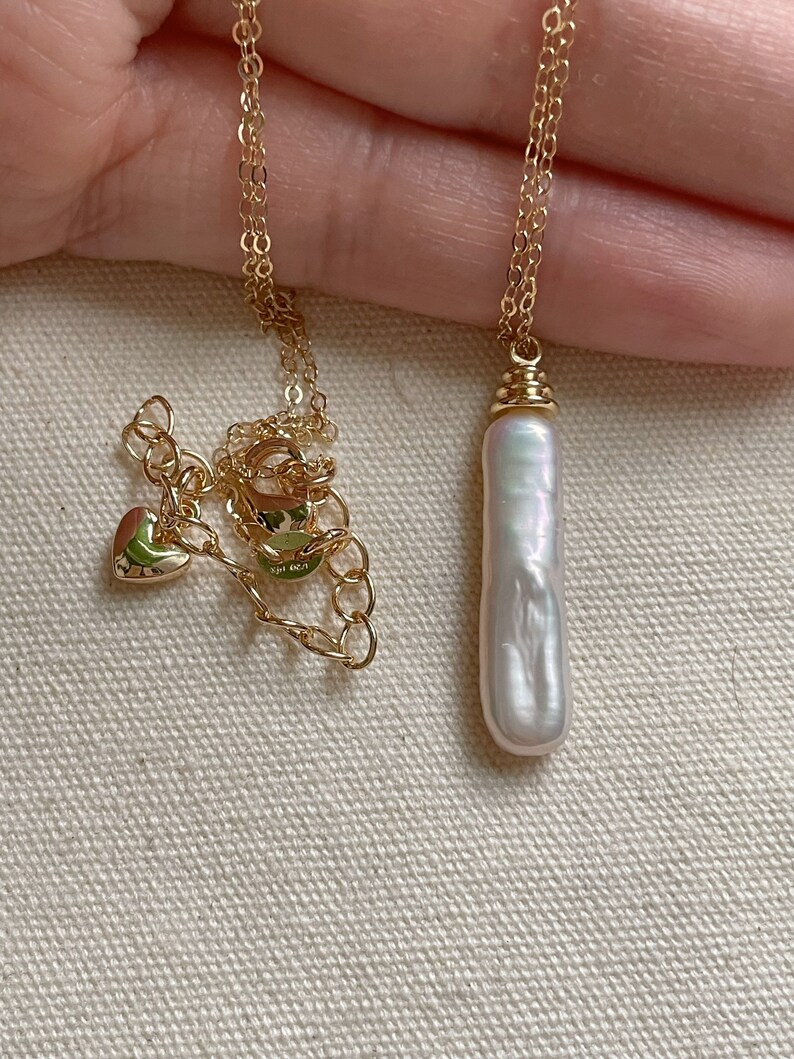 May include: A gold chain necklace with a large, white baroque pearl pendant.