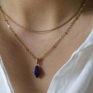 May include: A gold chain necklace with a dark blue gemstone pendant. The pendant is a faceted, teardrop shape.