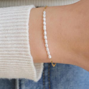 May include: A delicate gold chain bracelet with small white pearls. The bracelet is simple and elegant, perfect for everyday wear.