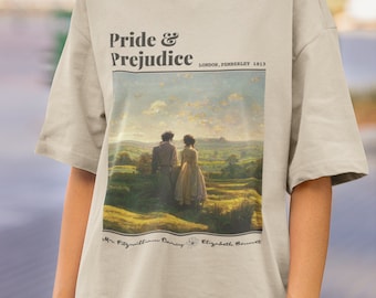 May include: A beige t-shirt with a graphic print of a painting depicting two people standing in a field. The text "Pride & Prejudice" is printed above the painting, along with the text "London, Pemberley 1813". The names "Mr. Fitzwilliam Darcy" and "Elizabeth Bennet" are printed below the painting.