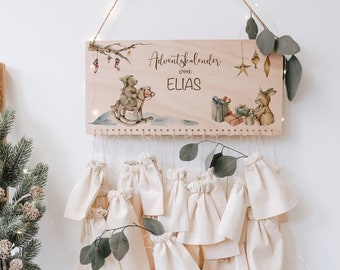 May include: A wooden Advent calendar with a personalized name "Elias" and a cute illustration of two bears riding a rocking horse. The calendar has 24 small fabric pouches hanging from it.