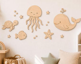 Könnte beinhalten: Ein Set aus hellen Holzwanddekorationen mit Meeresbewohnern, darunter eine Qualle, ein Wal, eine Schildkröte, ein Fisch und zwei Seesterne, ergänzt durch kleine kreisförmige und sternförmige Akzente, die an einer Wand angebracht sind.