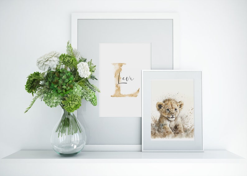 Elegante Bilderrahmen auf einem Regal präsentieren einen zauberhaften Aquarelldruck mit einem niedlichen Löwenbaby. Die sanften Farben und das zarte Design verleihen jedem Raum eine harmonische, naturverbundene Atmosphäre. Daneben steht ein frischer Blumenstrauß in einer Glasvase, der das Arrangement perfekt ergänzt und für einen Hauch von Eleganz sorgt. Ideal für Kinderzimmer oder Wohnzimmer.