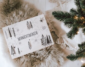 May include: A rectangular wooden sign with a Christmas theme. The sign features a pattern of stylized trees, snowflakes, and stars in black and gray. The German text "WEIHNACHTSWÜNSCHE" is printed in the center. The sign rests on a faux fur rug.