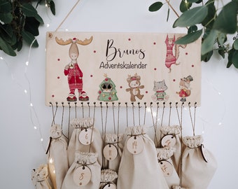May include: A wooden Advent calendar with the name "Bruno's Adventkalender" printed on it. The calendar features a moose, a Christmas tree, a bear, a cat, and a squirrel. There are 24 small fabric bags hanging from the bottom of the calendar, each with a number on it.