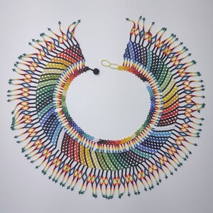 May include: A colorful beaded necklace with a fringe design. The necklace is made of small, colorful beads that are woven together in a intricate pattern. The fringe is made of long strands of beads that hang down from the bottom of the necklace.