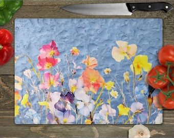 May include: A blue cutting board with a watercolor floral design featuring pink, yellow, and purple flowers. The flowers are arranged in a random pattern on the board.