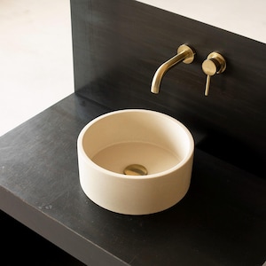 May include: A white ceramic vessel sink with a gold faucet and drain on a black countertop.
