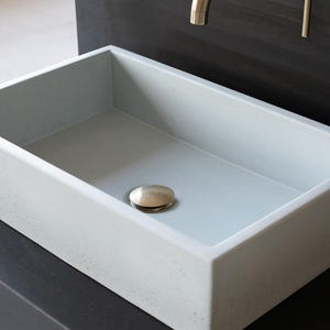 Peut inclure: Un évier rectangulaire en béton avec une finition gris clair et un bouchon de vidange argenté.