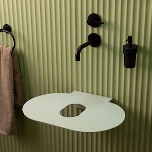 May include: A modern bathroom setup featuring a light green wall with vertical ridges. A black faucet, soap dispenser, and towel ring are mounted on the wall. A light green, oval-shaped shelf with a cutout is also mounted on the wall.