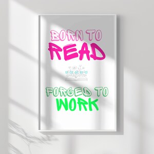 Könnte beinhalten: Ein weißer gerahmter Poster mit dem Text "Born to Read" in Pink und "Forced to Work" in Grün. Eine kleine Illustration eines Buches mit Blumen befindet sich zwischen den beiden Sätzen.