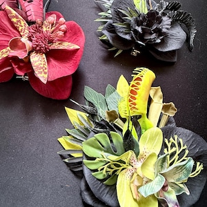 Könnte beinhalten: Drei Blumenarrangements aus künstlichen Pflanzen. Eines ist tiefrot mit gefleckten Blütenblättern, eines ist schwarz mit einer gelben Venusfliegenfalle und eines ist eine Mischung aus Schwarz, Limettengrün und Gelb mit einer Venusfliegenfalle und Monstera-Blättern.