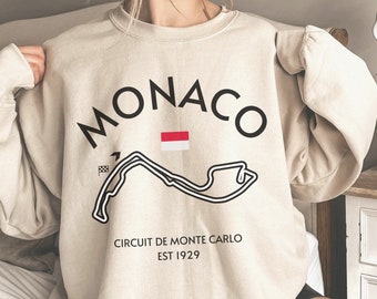 May include: A beige sweatshirt with a black graphic of the Monaco Grand Prix race track and the text "MONACO CIRCUIT DE MONTE CARLO EST 1929".
