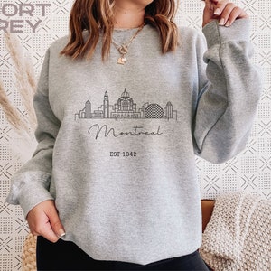 May include: A gray sweatshirt with a black outline of the Montreal skyline and the text "Montreal EST 1642".
