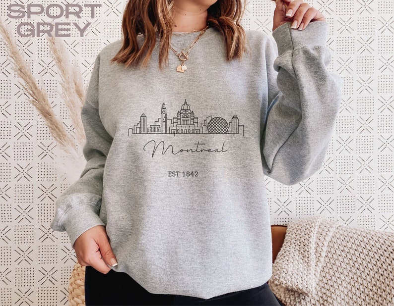 May include: A gray sweatshirt with a black outline of the Montreal skyline and the text "Montreal EST 1642".