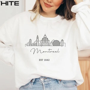 May include: White sweatshirt with a black line drawing of the Montreal skyline, including the words "Montreal" and "EST 1642".