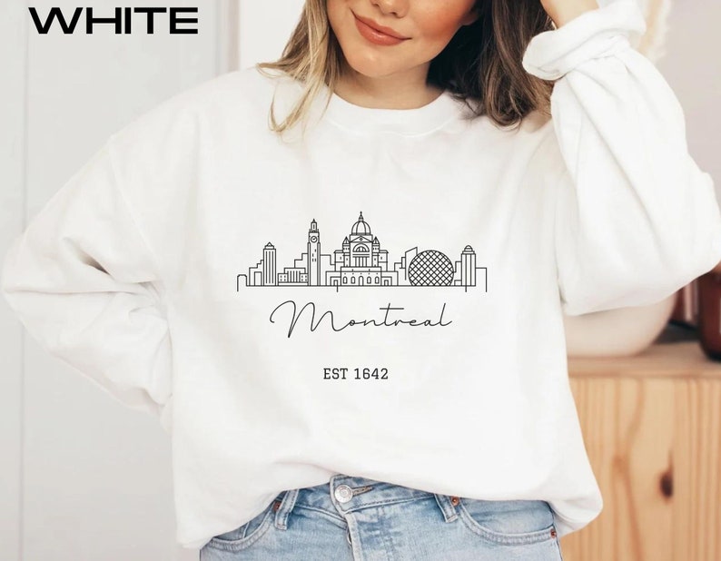 May include: White sweatshirt with a black line drawing of the Montreal skyline, including the words "Montreal" and "EST 1642".