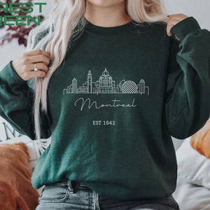 May include: Forest green sweatshirt with a white outline of the Montreal skyline, including the words "Montreal" and "EST 1642".