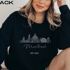 May include: Black sweatshirt with a white outline of the Montreal skyline and the text "Montreal EST 1642".