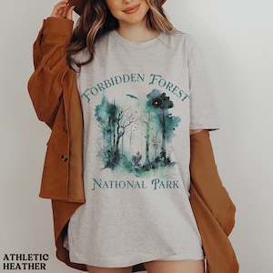 May include: A heather grey t-shirt with a watercolor design of a forest with the text "Forbidden Forest National Park" in teal blue.