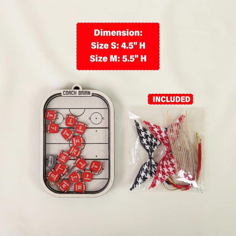 May include: A hockey-themed ornament with a wooden frame, featuring a miniature hockey rink and red jersey pieces. The ornament is 11.4 cm or 14 cm high. Included are decorative bow ties and hanging strings.