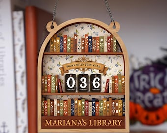 May include: Wooden bookshelf-shaped sign with a floral background and the text "BOOKS READ THIS YEAR." It has a counter showing "036" and the text "MARIANA'S LIBRARY." The sign is hanging by a chain.