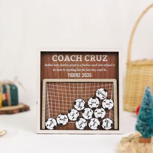 May include: A wooden soccer-themed display with a white frame. The display features a soccer goal and several soccer balls with names. The text "COACH CRUZ" and "TIGERZ 2025" are visible.