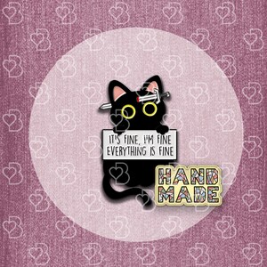 May include: Black cat enamel pin with a sword through its head, holding a sign that says "It's fine, I'm fine, everything is fine". The pin also has a "Handmade" label with a mosaic design.