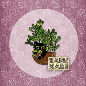 May include: Black cat peeking out of a brown pot with green plants and yellow flowers. The pot has the word "HANDMADE" written on it in colorful mosaic tiles.