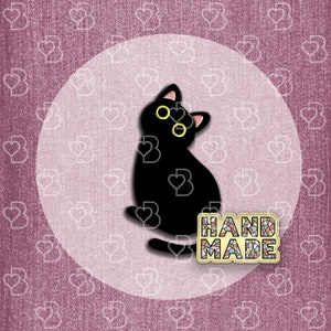 May include: Black cat pin with yellow eyes and the word "HANDMADE" in colorful mosaic letters.
