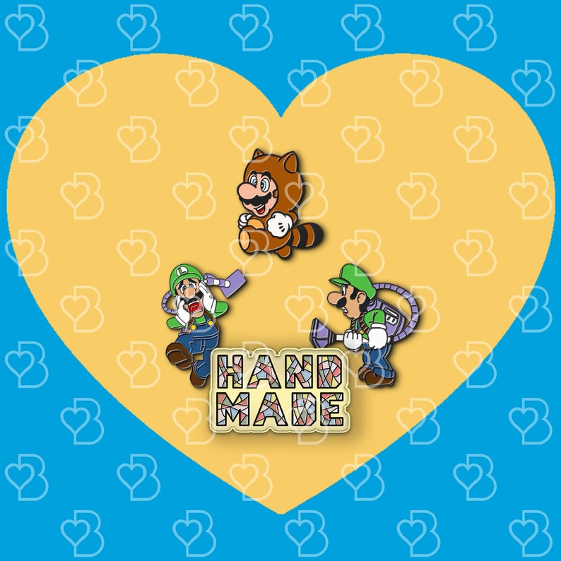 K&ouml;nnte beinhalten: Drei Emaille-Pins mit Figuren aus der Super Mario Bros. Videospielserie. Die Pins befinden sich auf einem gelben herzf&ouml;rmigen Hintergrund. Die Pins zeigen Mario, Luigi und einen Tanooki Mario. Der Text "HANDMADE" befindet sich in der Mitte des Bildes.