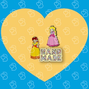 K&ouml;nnte beinhalten: Zwei handgefertigte Emaille-Pins mit Prinzessin Peach und Daisy aus der Super Mario Bros. Videospielserie. Die Pins sind gelb, pink und wei&szlig; mit schwarzen Umrissen. Der Text "HANDMADE" ist in bunten Mosaikfliesen.