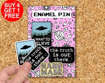 May include: Four enamel pins with a pink background. The pins feature a UFO, a planet, the text "the truth is out there", and the text "I want to believe". The pins are handmade and have a colorful mosaic design.