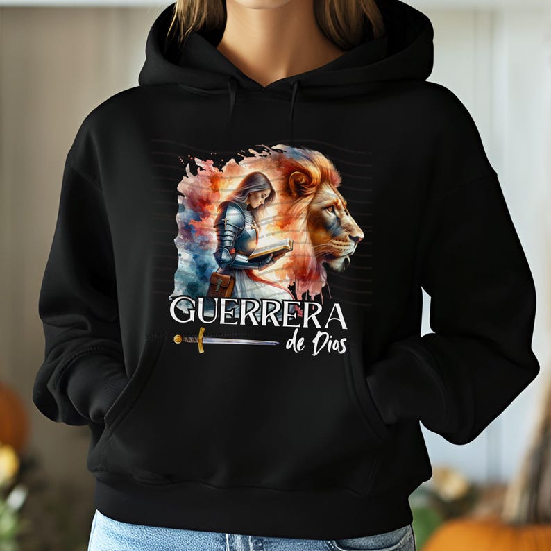 May include: Black hoodie with a watercolor illustration of a woman in armor holding a book, a lion, and the text "GUERRERA de Dios".