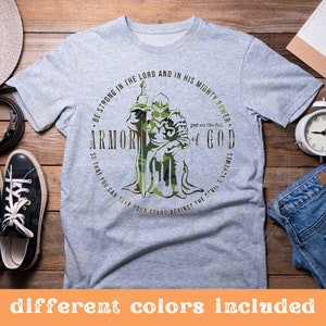 Puede incluir: Una camiseta gris con un dise&ntilde;o de camuflaje de un caballero sosteniendo una espada. El texto en la camiseta dice "S&eacute; fuerte en el Se&ntilde;or y en su poder&iacute;o. Ponte la armadura completa de Dios para que puedas resistir los planes del diablo."
